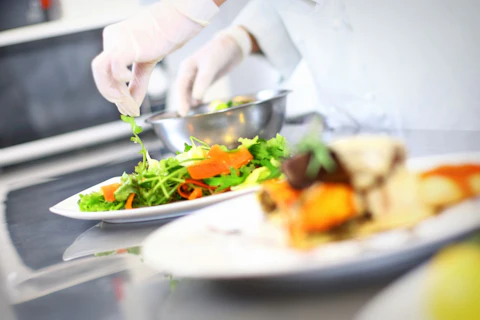 Zbliżenie na kucharza w białym stroju i rękawiczkach przygotowującego posiłki na talerzach.